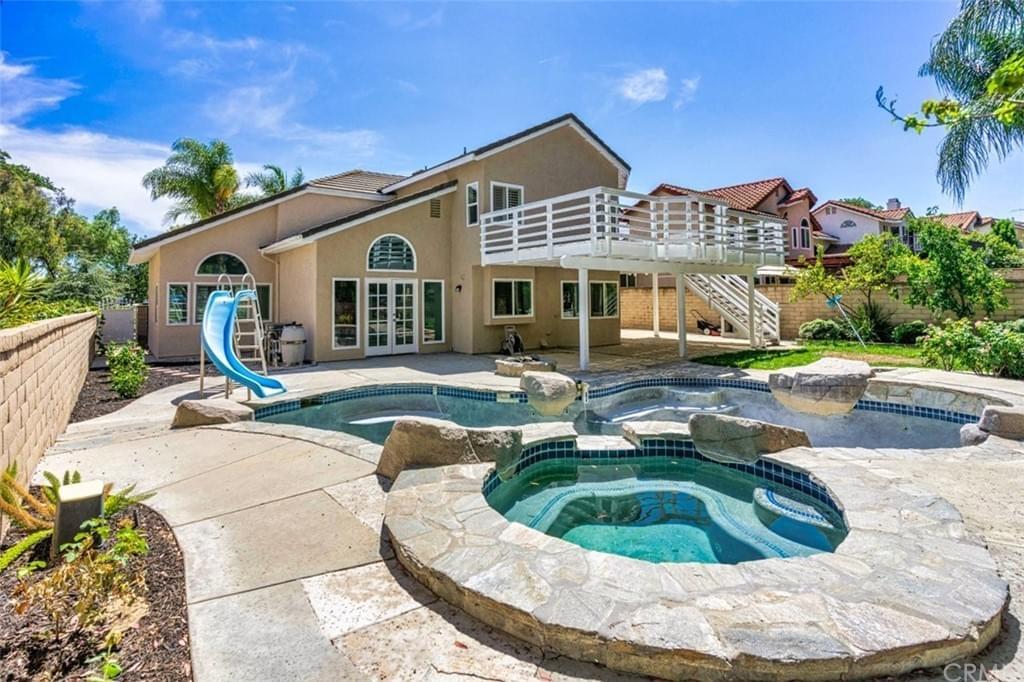 Backyard oasis of a large home featuring a second-story deck and stone patio, large pool, spa, and slide